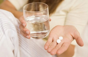 Стакан воды и таблетки в руке у женщины
